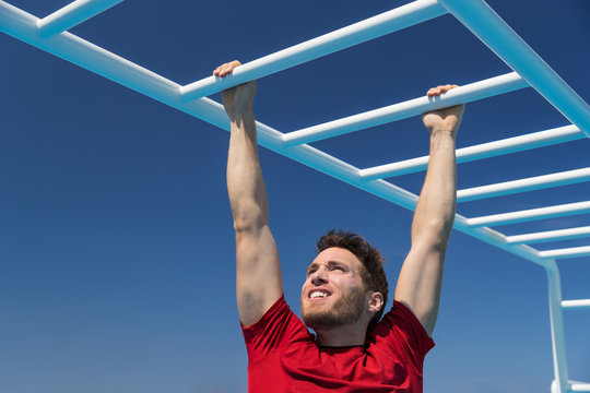 Fitness monkey bars man training arms muscles on jungle gym outdoors in summer. Athlete working out gripping climbing on ladder equipment at sport athletics centre.