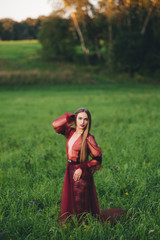 A beautiful young woman in a bard dress is gazing on in the field and the garden.