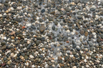 Close-up view of wet pebble in foam bubbles as background.