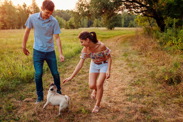 Young couple walking pug dog in autumn forest. Happy puppy running along and having fun playing...