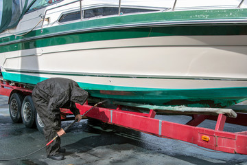 man wearing black waterproof rain suit while cleaning power boat hull with pressure washer