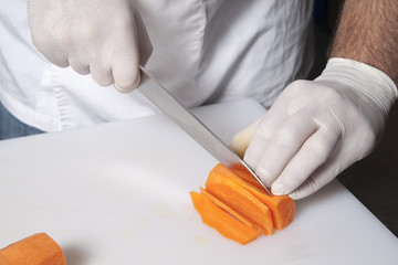 the chef in gloves cuts carrots on a plastic board