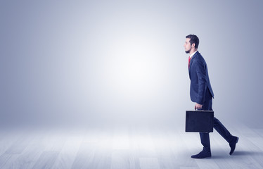 Obraz premium Successful businessman walking in front of an empty wall with briefcase on his hand 