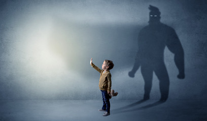 Fototapeta premium Cute kid in a room with plush on his hand and hero shadow on his background 