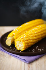 Sweet corn on cob with maldon salt, steaming. Dark wooden plate, high resolution.