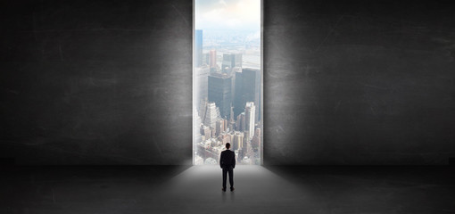 Businessman standing in a dark room and looking outside to a cityscape view
