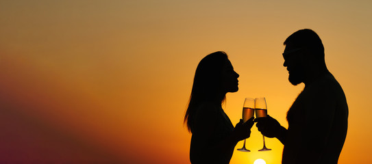 loving couple drinking wine or champagne during sunset time, silhouette of a couple with wineglasses on sunset background, man and woman, looking each other,  and holding in their hands glasses .