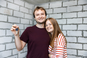 Young smiling couple showing keys to new home hugging looking at camera