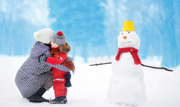 Little Boy With His Mother/babysitter/grandmother Building Snowman In Snowy Park