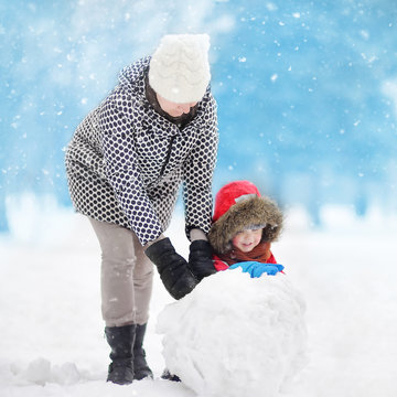 Little Boy With His Mother/babysitter/grandmother Building Snowman In Snowy Park