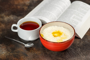 Oatmeal porridge in bowl, tea and book