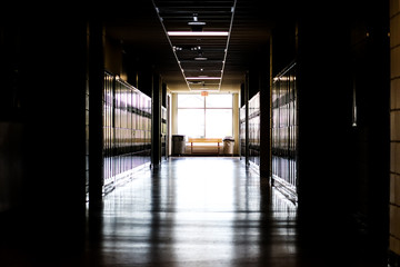 Straight view of darkly lit hallway with bright light at end and lockers covering the walls on either side 