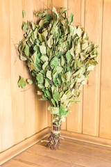 Green birch broom stands on a shelf in the corner of the bath