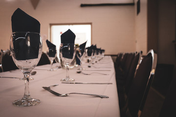 Wide view of celebratory hall with long cloth covered tables, chairs, and place settings