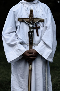 Hands gently holding onto religious items while wearing white robes and hanging crucifix