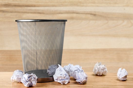 Trash can with paper sheets on wooden desk