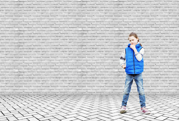 Fototapeta na wymiar Little girl stands in thoughtfulness by the high white brick wall
