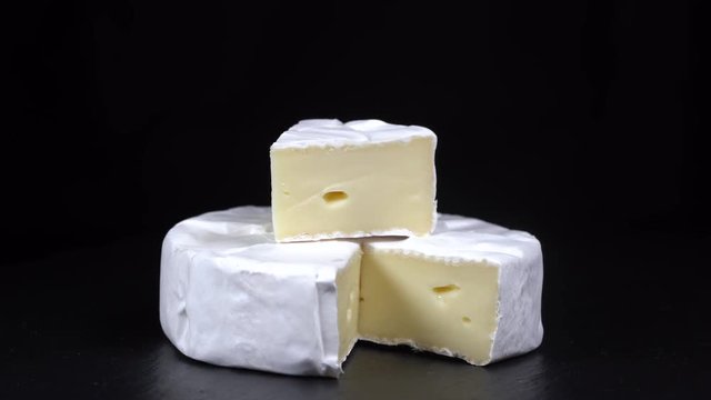 Rotation cheese Camembert on black slate plate. Delicious piece of white cheese Camembert on black background, close up, macro