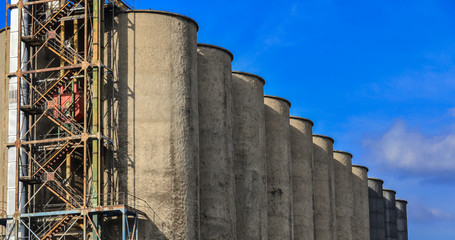 line of seven cement grain storage silos against blue sky © MJCavenagh