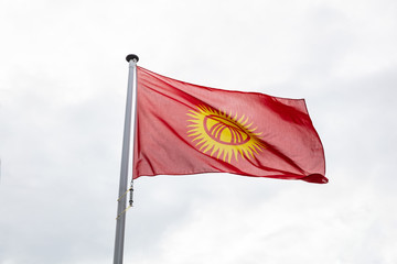 Kyrgyzstan flag on a pole waving, cloudy sky background