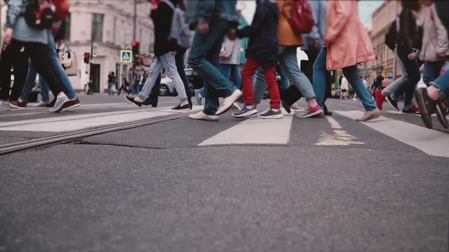 Low angle slow motion shot of people's legs and feet crossing a busy city street, red bicycle passing close by camera.