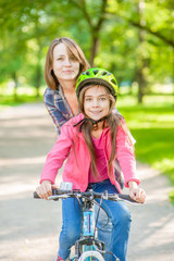 Obraz premium Smiling mother teaches her daughter to ride a bicycle in the park