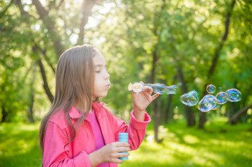 A little girl blowing soap bubbles in summer park