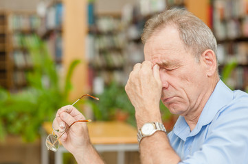 Senior man having a headache in library
