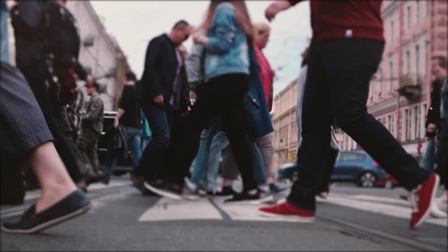 Beautiful slow motion shot of people's legs and feet walking across a busy old city street with tram rails in the middle