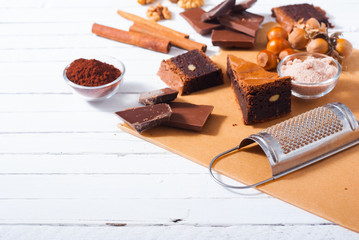 chocolate brownie cake and ingredients, baking papaer on white wood table background
