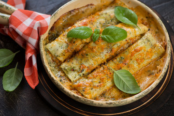 Closeup of cannelloni baked with spinach and cheese and topped with fresh green basil leaves, studio shot