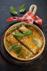 Cannelloni with spinach and cheese filling in a baking pan, vertical shot over dark brown stone background