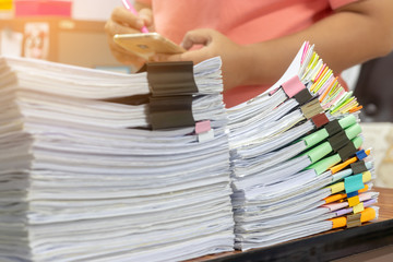 Teacher is checking student homework assignment and report on table in office for score. Unfinished paperwork stacked in archive with colorful papers and paper clips. Education and business concept.