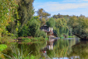 Obraz premium Old wooden pier with boats on small river against green trees. River landscape at sunny autumn morning