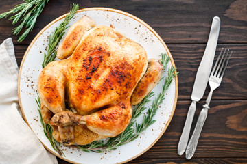 Whole grill chicken with caramelized skin and fresh rosemary on a wooden dinner table.