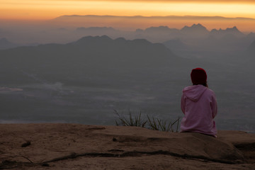 Obraz premium Woman sitting serenely of the cliff and looking at the valley and mountains in the morning