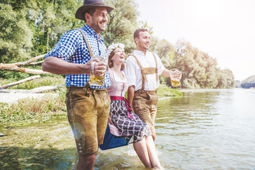 Oktoberfest Freunde in Lederhosen und Dirndl trinken Bier an der Isar