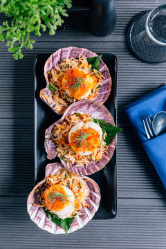 Top view of scallop in shell with spicy pomelo salad served in black plate.
