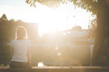 Junge Frau sitzt in urbaner Gegend auf Mauer und blickt dem Sonnenuntergang entgegen, Vitamin D