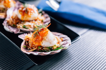 Close up Grilled scallop in shell with spicy pomelo salad served in black plate.