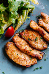 Close up BBQ grilled chicken breast with salad served in blue plate on wooden table.