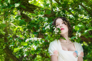 Young woman in an long white bride dress in flowers tree