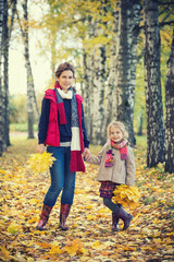Naklejka na ściany i meble Smiling little girl and her mother enjoy walk in autumn park and play with bright autumn leaves