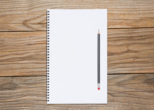 Blank page of a sketchbook with a black pencil over old wooden texture