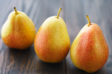 Three fresh pears on a dark wooden background. Backlight, selective focus, high resolution.