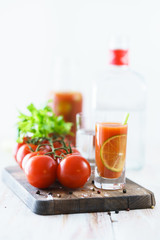 Sangrita in a shot glass served with fresh tomatoes, celery sticks and black pepper. Tequila bottle in bokeh, wooden board, high resolution.