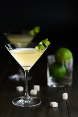 Two daiquiris served in cocktail glasses, garnished with lime zest. Dark wooden background, high resolution.