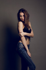 Fototapeta premium Young brunette female in black bra jeans and leather jacket over grey background