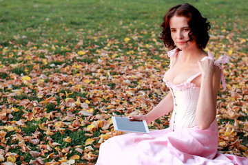 Fine emotional brunette with tablet pad sitting on the grass in autumn. Copy space. Yonge girl in...