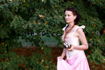 Fine emotional brunette with vintage photo camera. Yonge girl in vintage pink pastel with live expressions on beautiful country and old background.